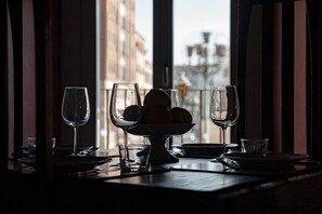 Una mesa de comedor con copas de vino y un frutero, frente a una ventana con vistas a la ciudad.
