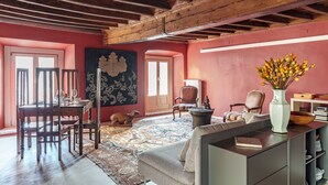 Una habitación con techo de madera, una mesa de comedor con sillas, un sofá, un cuadro grande, un jarrón con flores y una estantería.