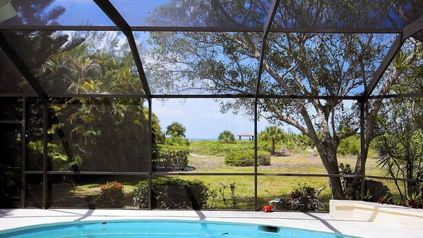 A swimming pool with a view of a tropical landscape, enclosed by a metal structure. - Rue Belle Mer (Sanibel)