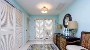 A hallway with a patterned rug, a wooden bench, a mirror, and a lamp on a console table. - Rue Belle Mer (Sanibel)