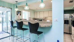 A kitchen with a bar area, bar stools, and a refrigerator. - Rue Belle Mer (Sanibel)