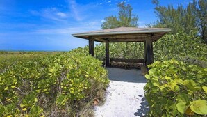 A wooden gazebo with a sloped roof, surrounded by dense green vegetation and a clear blue sky. - Rue Belle Mer (Sanibel)