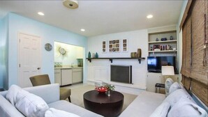 A living room with a sofa, a coffee table, a fireplace, a television, and a bookshelf. - Rue Belle Mer (Sanibel)