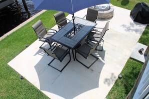 An outdoor patio with a table and chairs, a blue umbrella, and a fire pit. - Riverfront Retreat-Private Dock; Fishing, Boating & Peaceful Getaway in Welaka (Welaka)