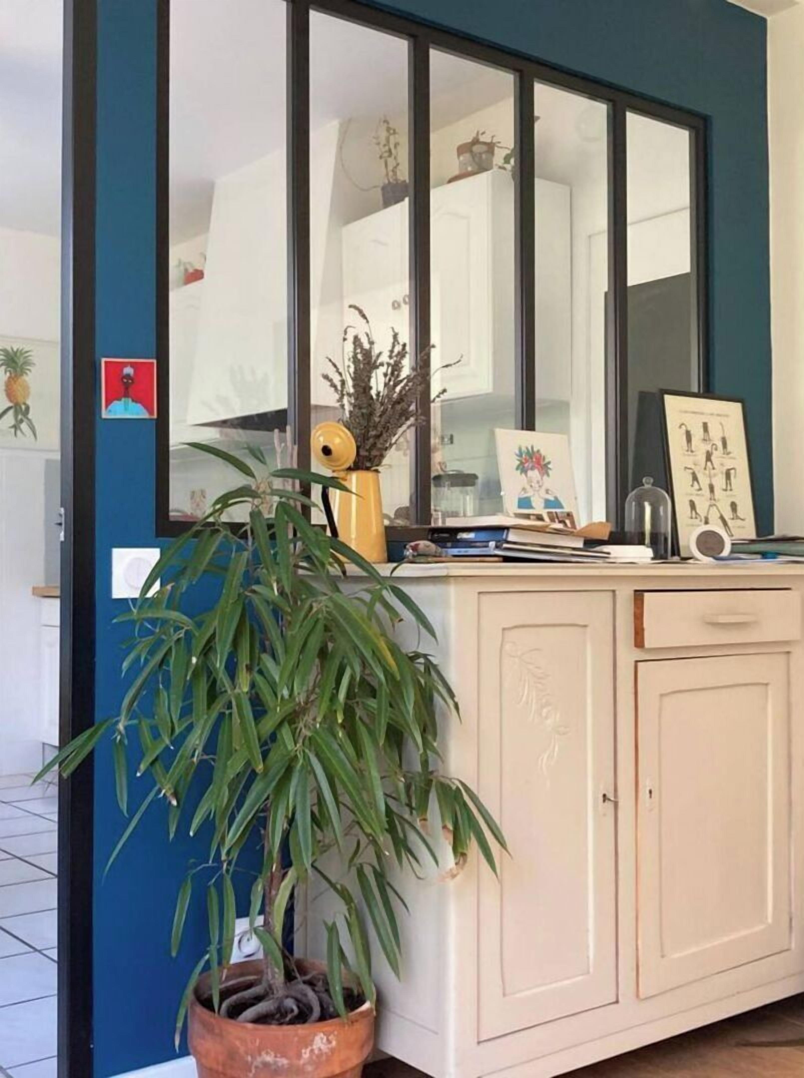 Une cuisine dotée d’une grande fenêtre, de placards, d’une plante en pot et de divers ustensiles de cuisine.