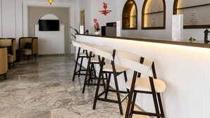 A bar area with a long counter, multiple stools, and hanging pendant lights. - One Resort Jockey (Monastir)