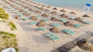 A beach with rows of sun loungers and thatched umbrellas. - One Resort Jockey (Monastir)