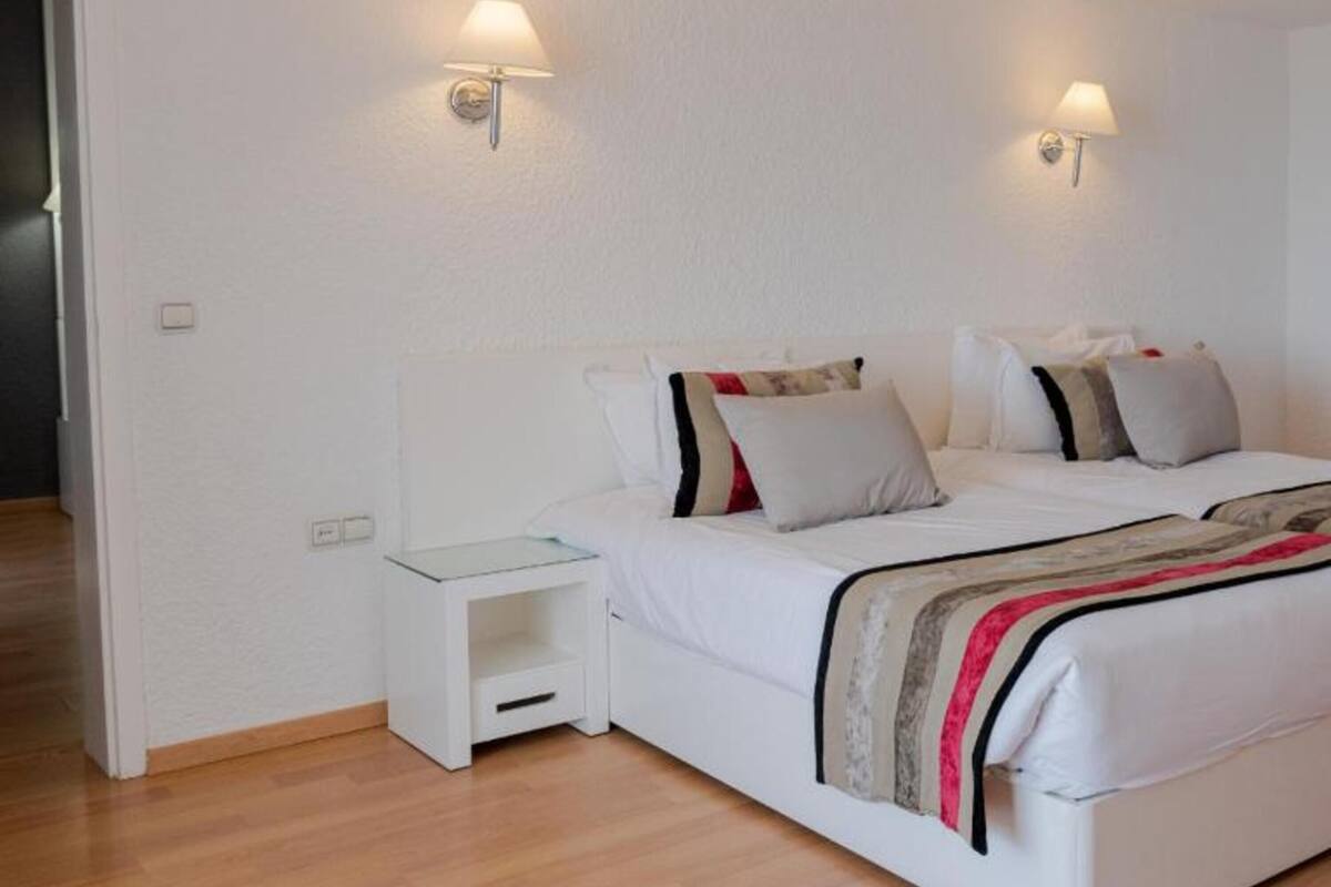 Quarto com cama, mesas de cabeceira e luzes fixadas na parede.