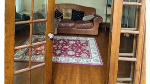 Ein Zimmer mit Holztür, braunem Ledersofa, Teppich mit rotem Muster und einem Bild an der Wand.