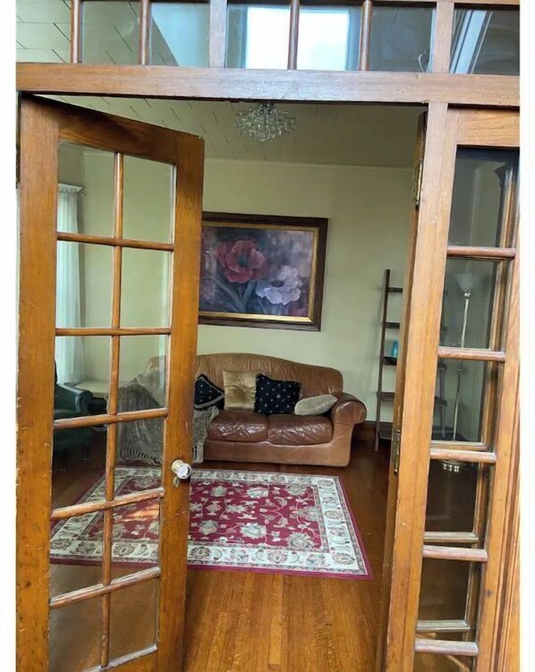 A room with a wooden door, a brown leather sofa, a red patterned rug, and a painting on the wall.