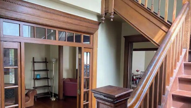 Eine Holztreppe führt zu einer zweiten Etage, eine Holztür mit Glasfeldern und ein gemustertes Teppich.