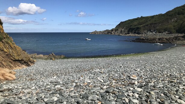 Uma praia de seixos com um litoral rochoso e um pequeno barco na água.