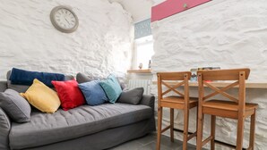 Uma sala de estar aconchegante com um sofá cinza, almofadas coloridas, uma cadeira de madeira e um relógio de parede.