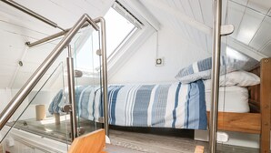 Quarto estilo loft com cama beliche, um banco de madeira e guarda-corrimão de vidro.