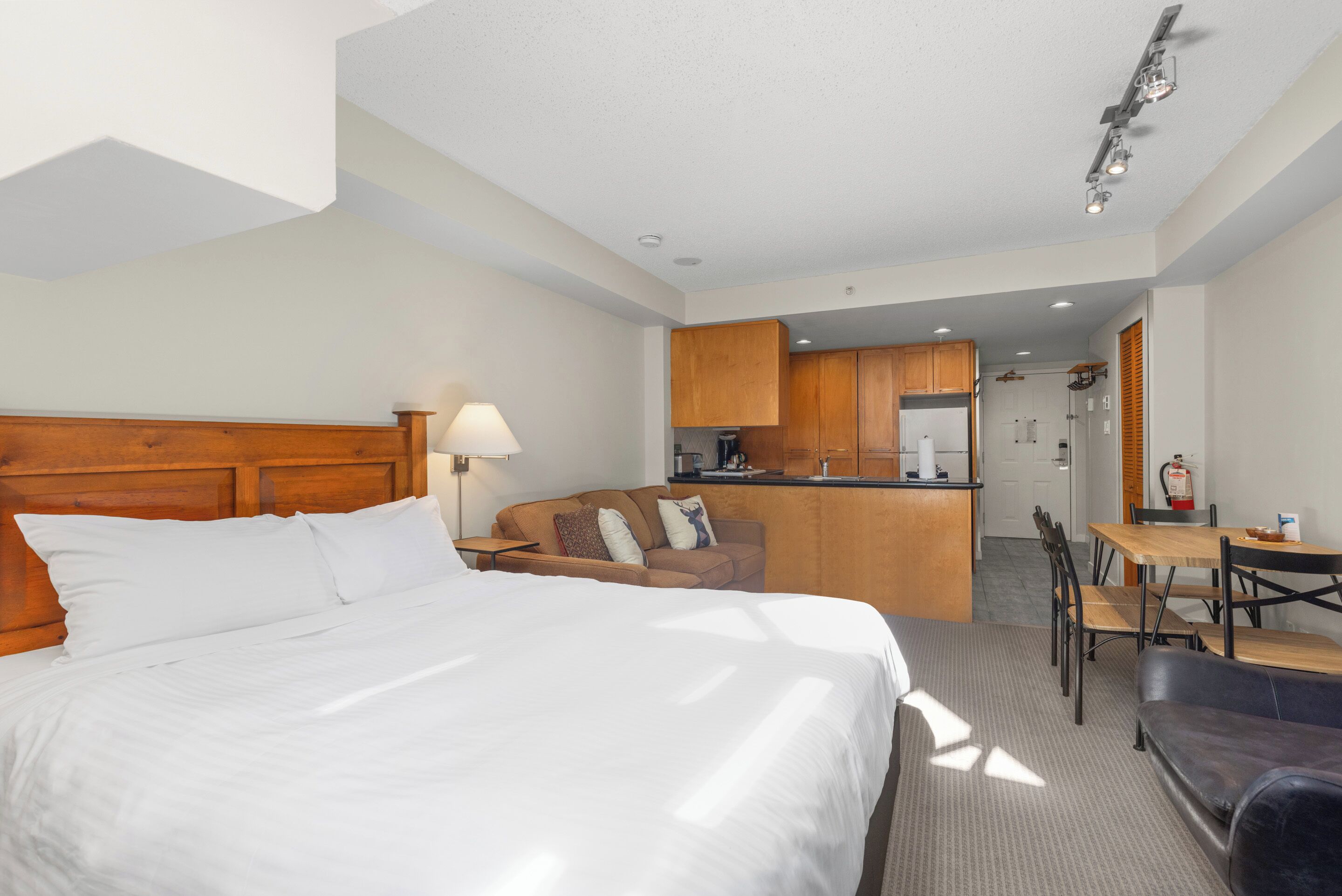 A hotel room with a bed, a sofa, a dining table, and a kitchenette.