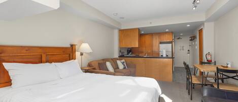 A hotel room with a bed, a sofa, a dining table, and a kitchenette.