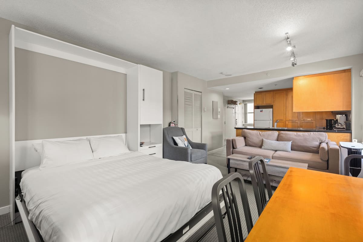 A hotel room with a bed, a dining table, a sofa, and a kitchenette.