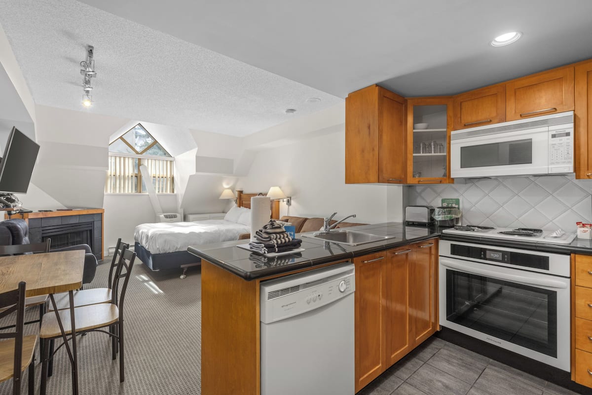 A compact kitchen with a dishwasher, oven, microwave, and wooden cabinets.