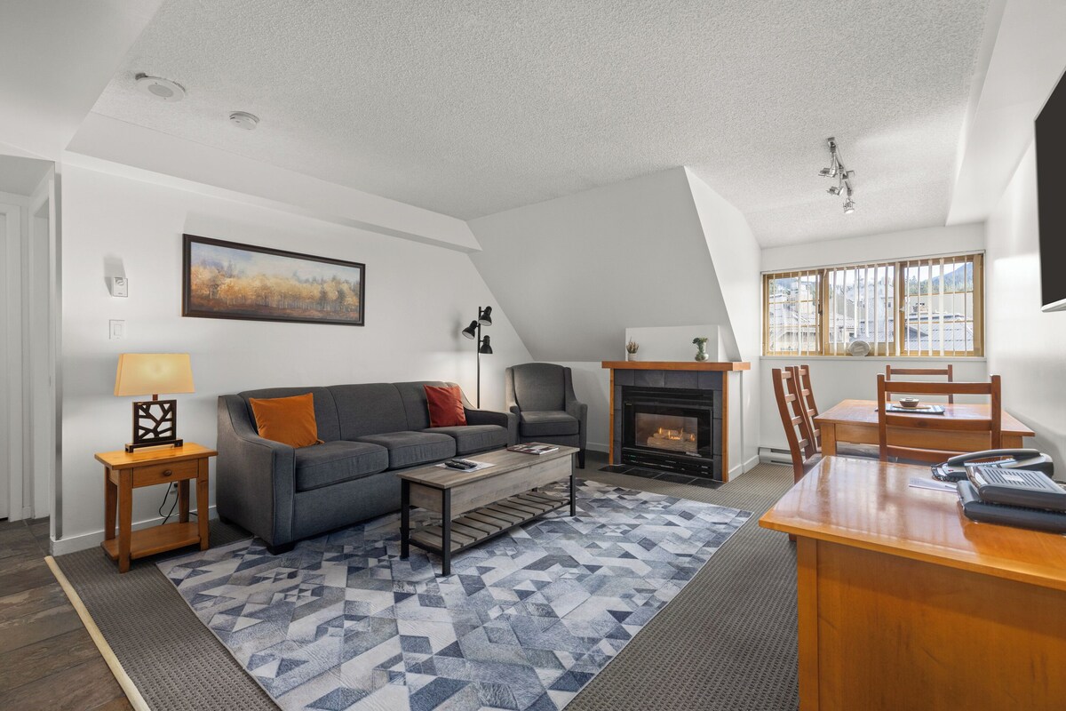 A living room with a sofa, coffee table, fireplace, and dining area.