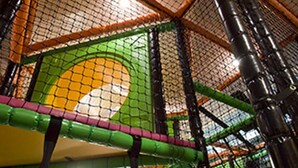 An indoor play area with netted walls, a green slide, and a yellow circular structure.
