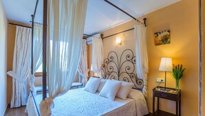 A bedroom with a four-poster bed, a nightstand with a lamp, and a painting on the wall.