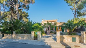 A Mediterranean-style villa with a stone entrance, lush greenery, and a clear blue sky.