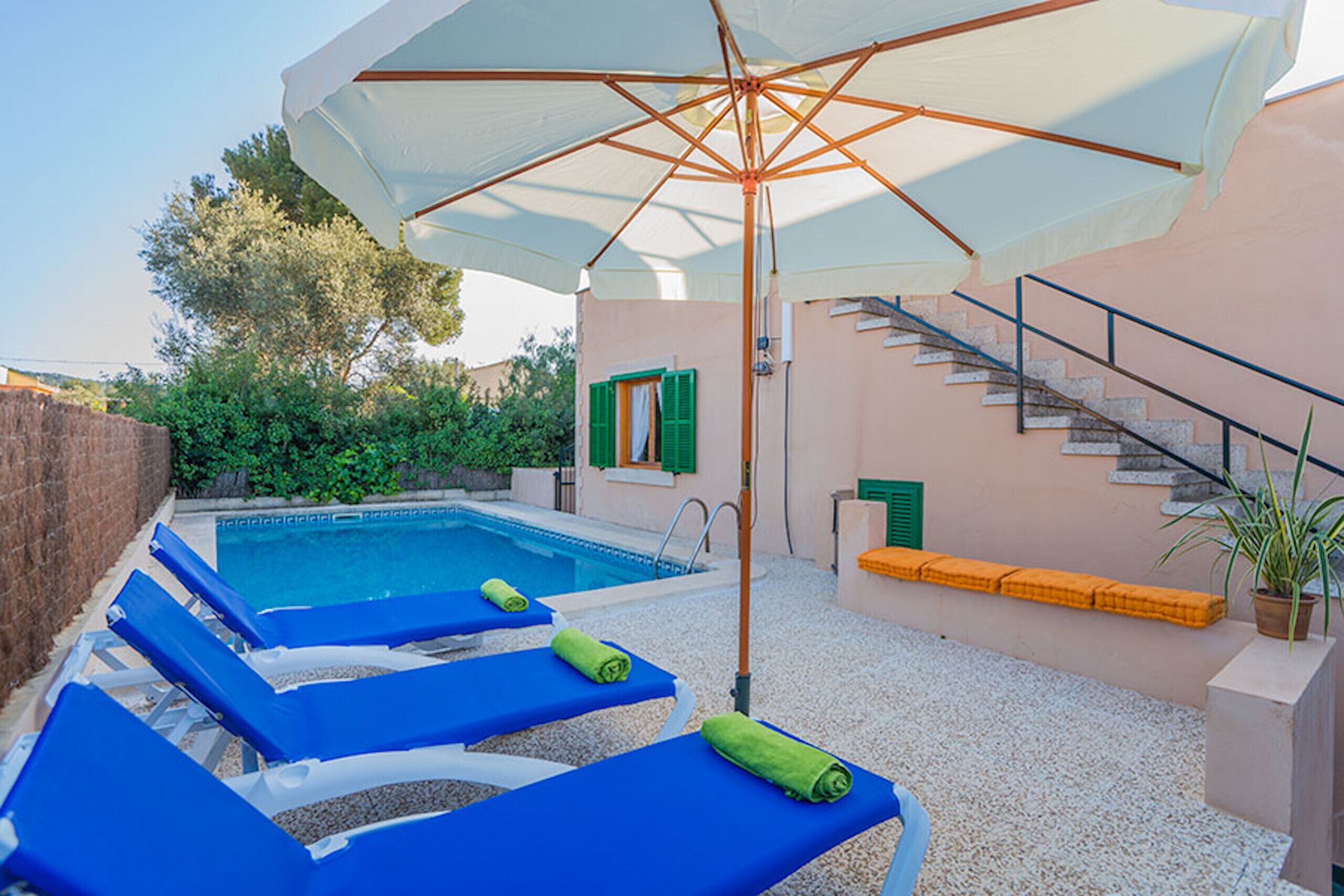A poolside area with lounge chairs, a large umbrella, and a staircase leading to an upper level.