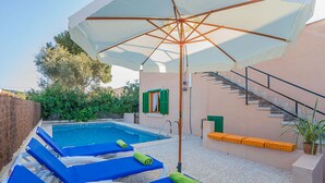 A poolside area with lounge chairs, a large umbrella, and a staircase leading to an upper level.