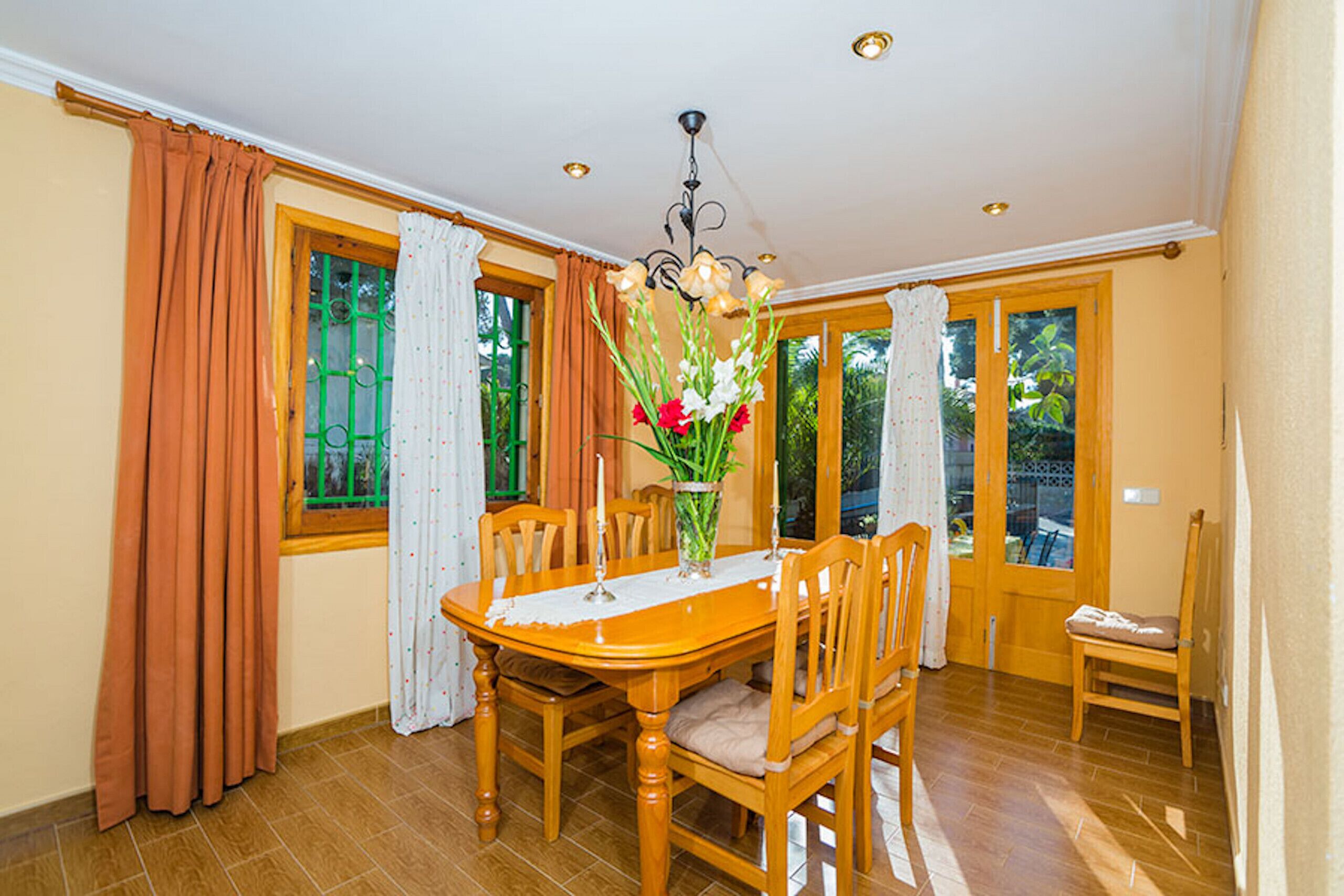 A dining room with a wooden table, chairs, a vase with flowers, and a chandelier.