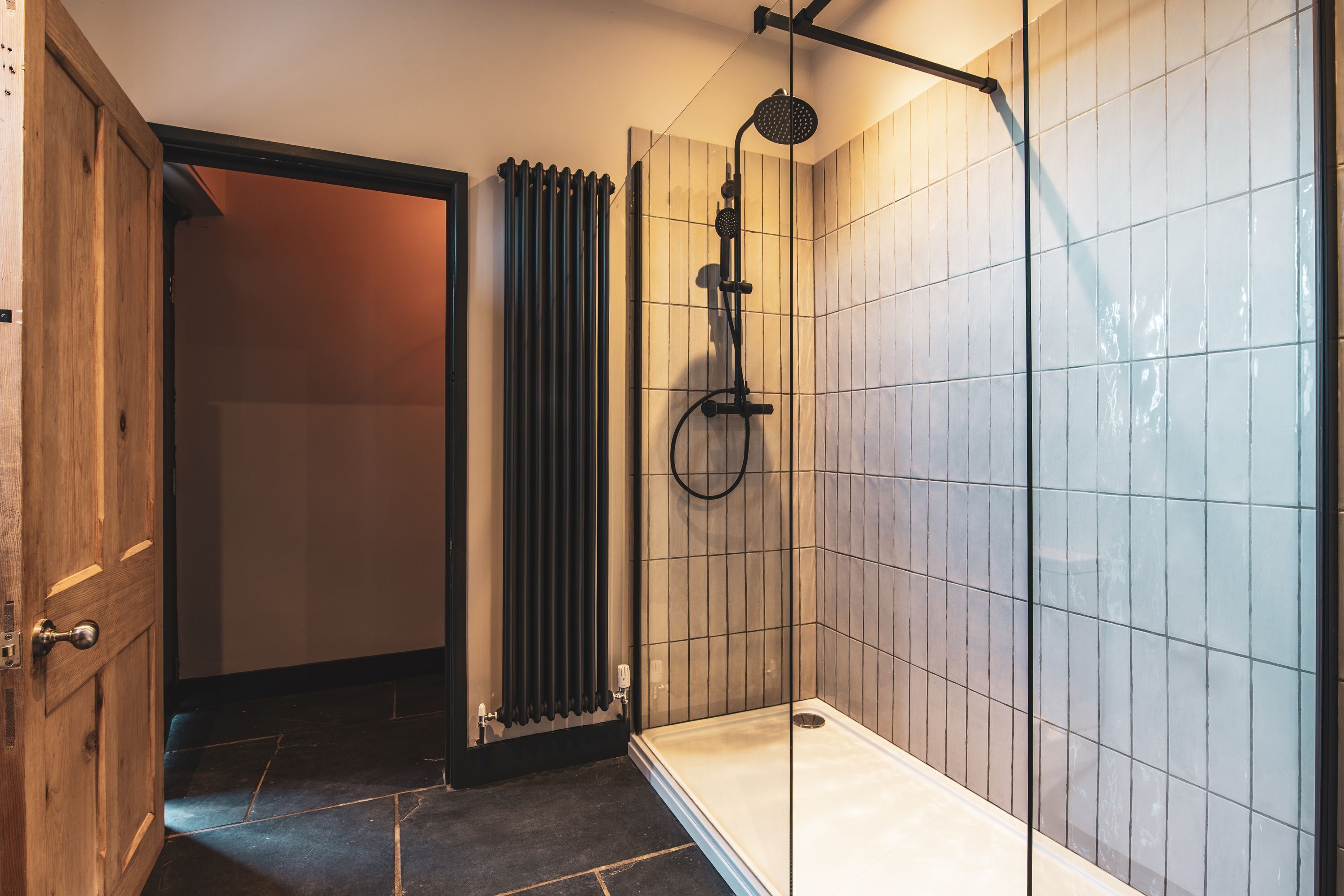 A modern bathroom with a glass shower enclosure, a radiator, and a wooden door.