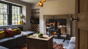 Een gezellige woonkamer met een open haard, een bank, een salontafel en een raam met uitzicht op bomen.