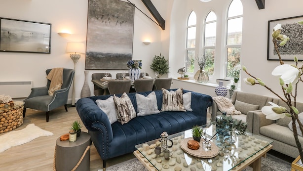 A modern living room with a blue sofa, dining table, and large windows. - Pilgrims Loft (Ventnor)