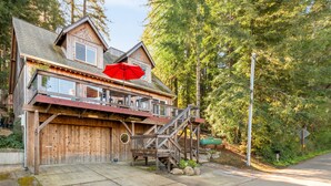 Une cabane en bois avec un grand garage, un balcon agrémenté d’un parasol rouge et un escalier menant à l’étage supérieur.