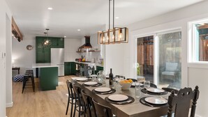 Une cuisine moderne avec un coin repas aménagé pour six personnes. Elle comprend un îlot central, des meubles de couleur verte et un luminaire suspendu.