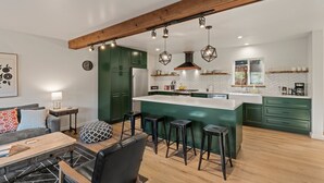 Une cuisine moderne avec des armoires vertes, une poutre en bois au plafond et des luminaires suspendus.