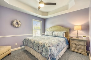 Une chambre à coucher comprenant un lit, une table de chevet, une lampe, une commode, une fenêtre et un ventilateur de plafond.