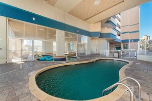 Une piscine intérieure avec des parois en verre transparent, une terrasse carrelée et un espace au bord de la piscine aménagé avec des chaises longues.