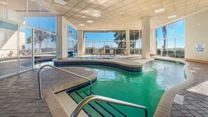 Una piscina interior con paredes de vidrio transparente, un borde de azulejos y un cartel que indica agua poco profunda y prohibido bucear.