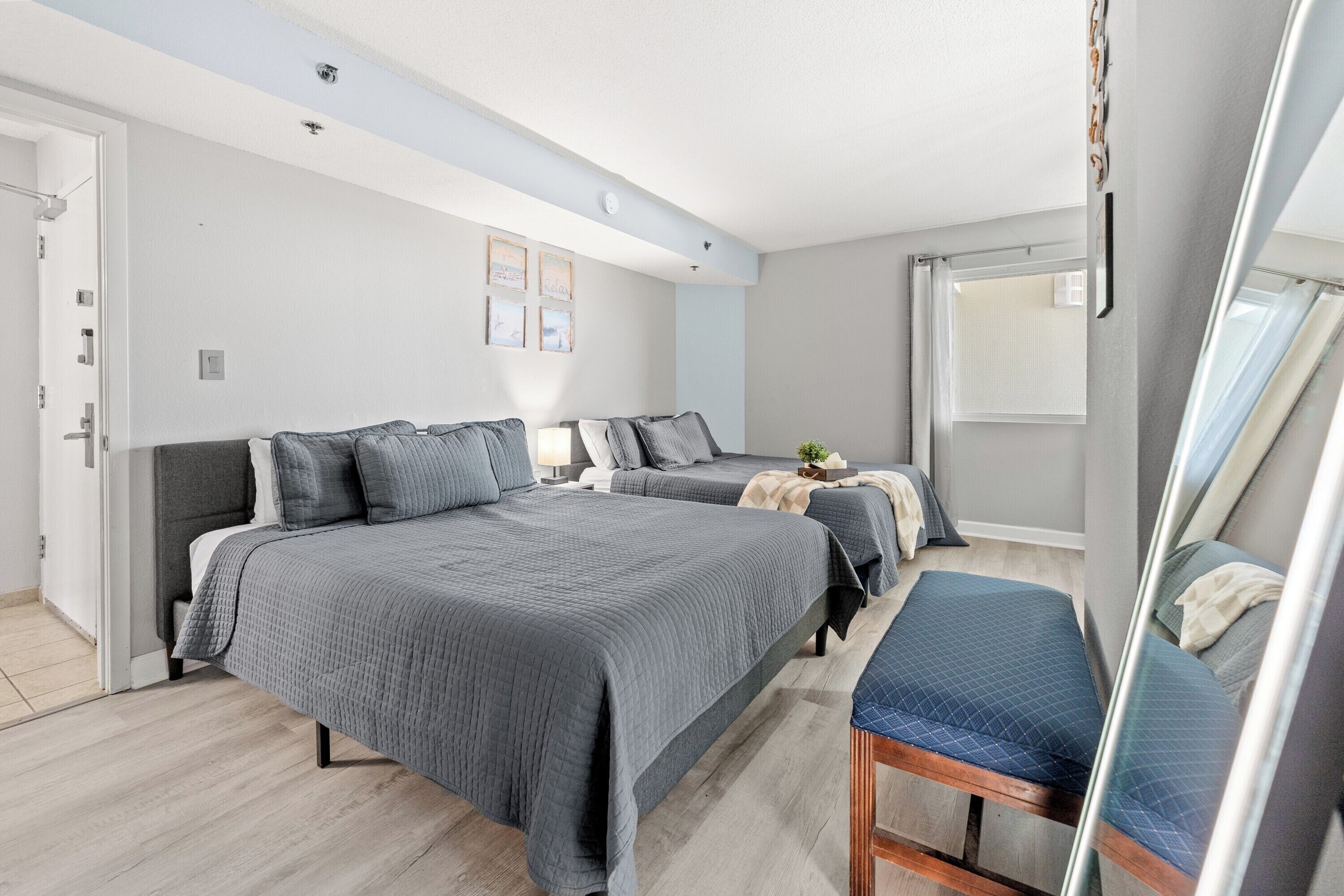 A bedroom with a large bed, two smaller beds, a chair, and a window with curtains.
