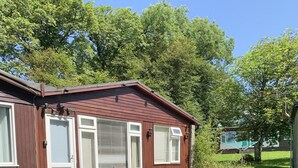 Ein eingeschossiges Holzhaus mit Veranda, einer Tür und einem Fenster mit Rollläden.