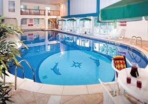 Une piscine intérieure dont le sol est décoré de motifs de dauphins, entourée de chaises longues et de parasols.