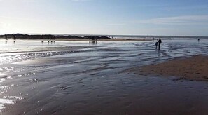 Une plage avec du sable mouillé et des gens qui se promènent le long du rivage.