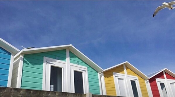 Une rangée de cabanes de plage aux couleurs vives, avec des bordures blanches, sous un ciel bleu azur.