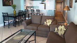 Una sala de estar con un sofá marrón, una mesa de centro de vidrio y una zona de comedor con sillas y una mesa.