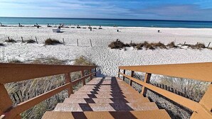 Una playa con una escalera de madera que baja a la arena, rodeada por una valla.