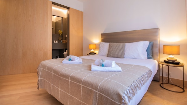 A hotel room with a large bed, two bedside lamps, a wooden headboard, and a mirror above the bed.