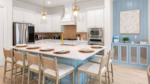 A modern kitchen with white cabinetry, stainless steel appliances, and a central island with bar stools.