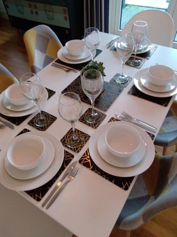 A dining table set with white plates, bowls, and wine glasses, with geometric patterned placemats.