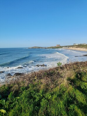 A coastal landscape with a beach, waves, and a building in the distance.
