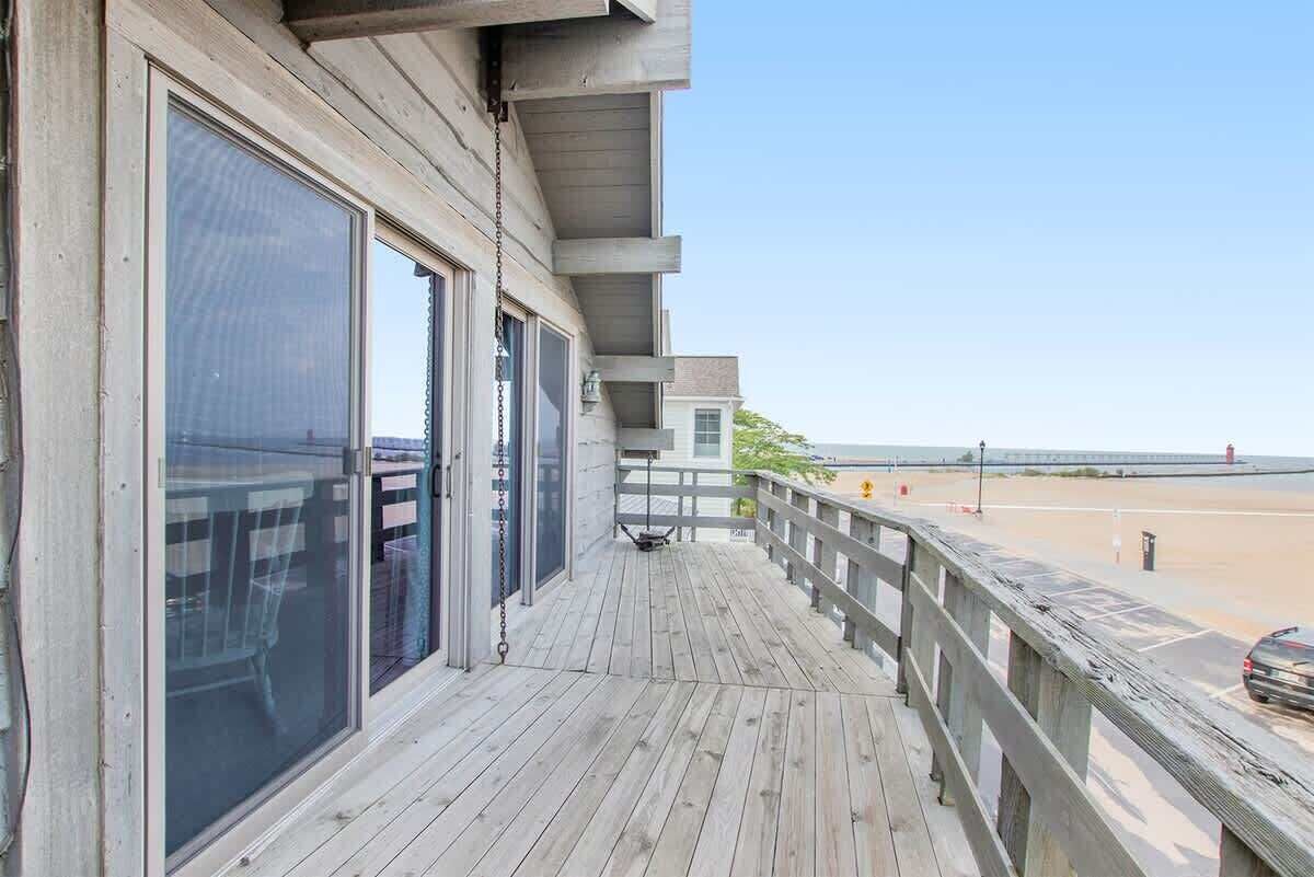 A wooden deck with large sliding glass doors, a metal railing, and a view of the beach.